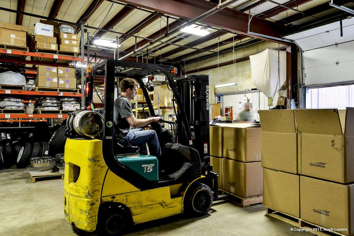 A forklift being used to move multiple boxes of aircraft brakes and aircraft wheels